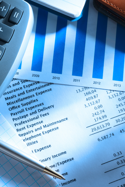 A close-up of a financial report with blue bar charts, a calculator, a pen, and a leather wallet on a desk.