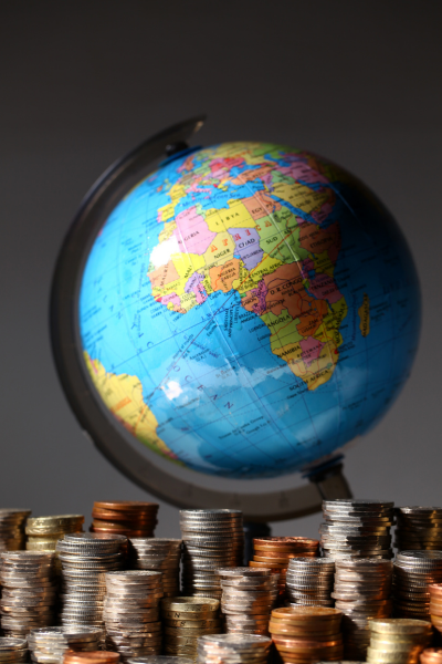 A desk globe surrounded by multiple stacks of various coins, symbolizing personal wealth and global financial planning.